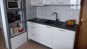Une cuisine compacte avec des meubles blancs, un plan de travail noir, un four à micro-ondes encastré, une machine à café et un panier à fruits.
