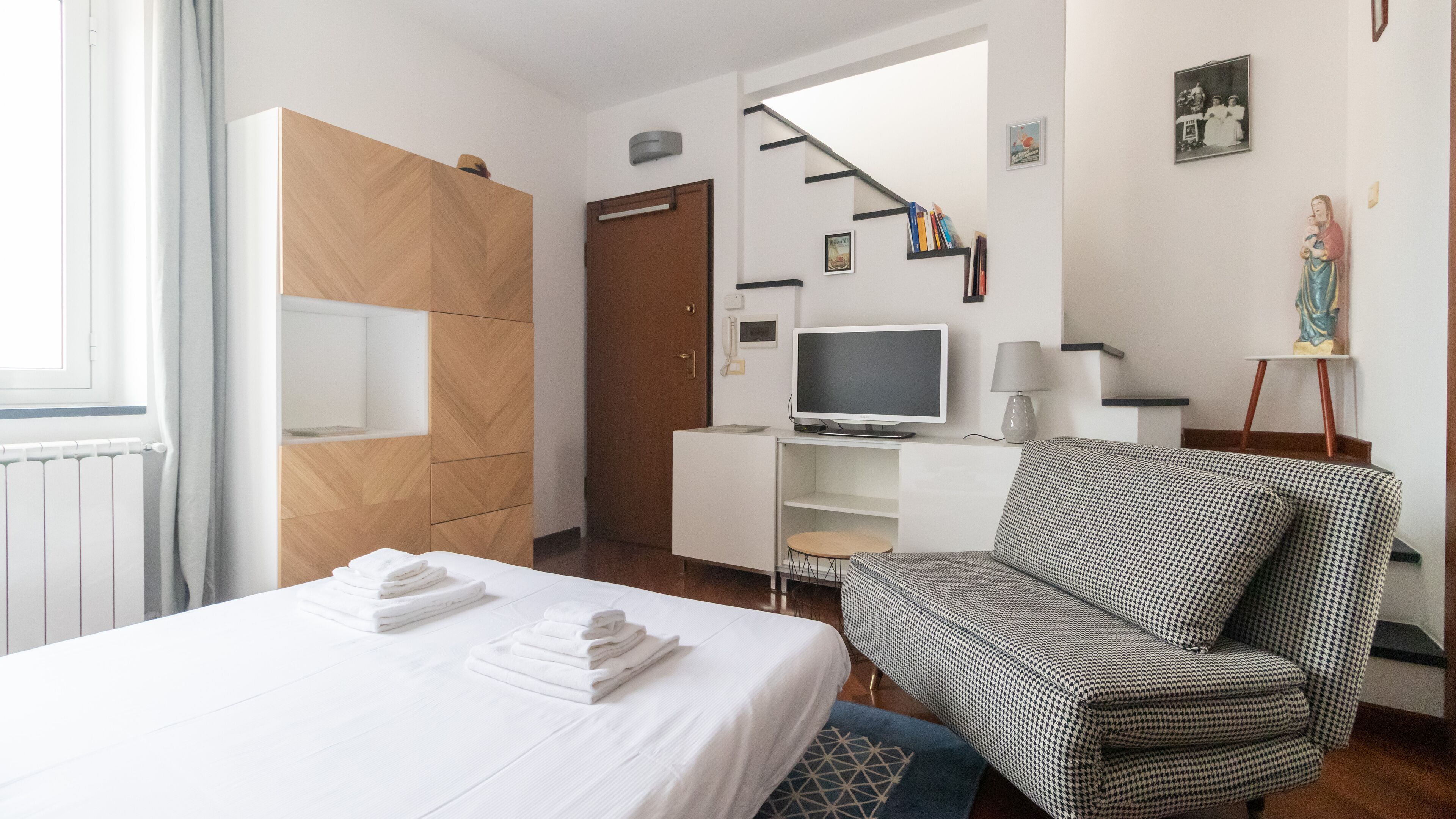 Ein Hotelzimmer mit einem Bett, einem Hounds-Tooth-Sessel, einem Fernseher und einem Schreibtisch mit Lampe.