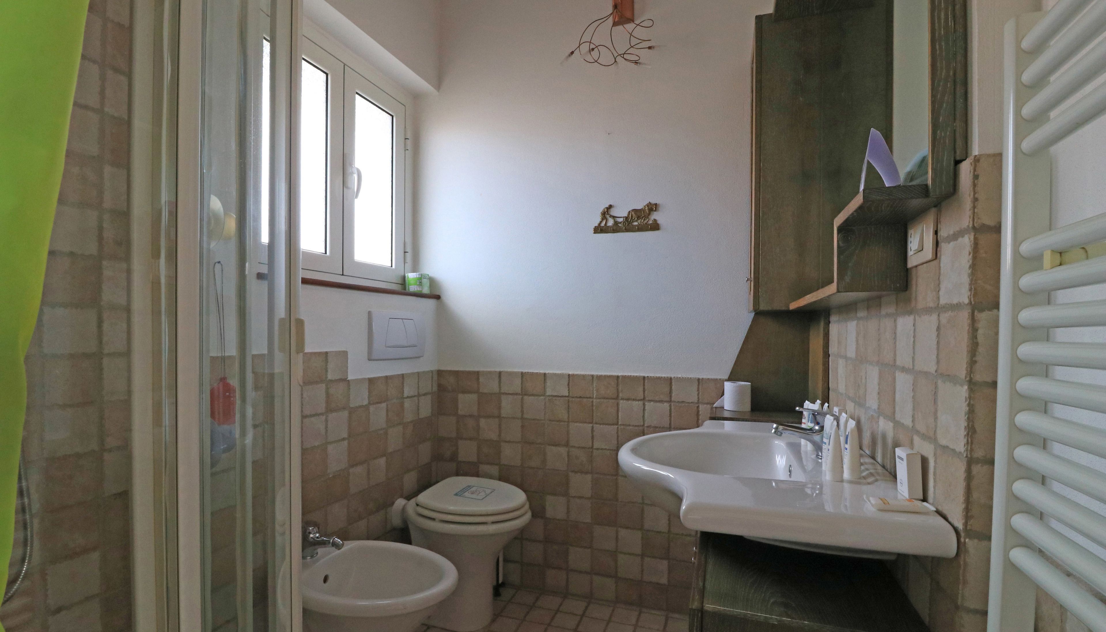 A small bathroom with a toilet, bidet, sink, and a window.