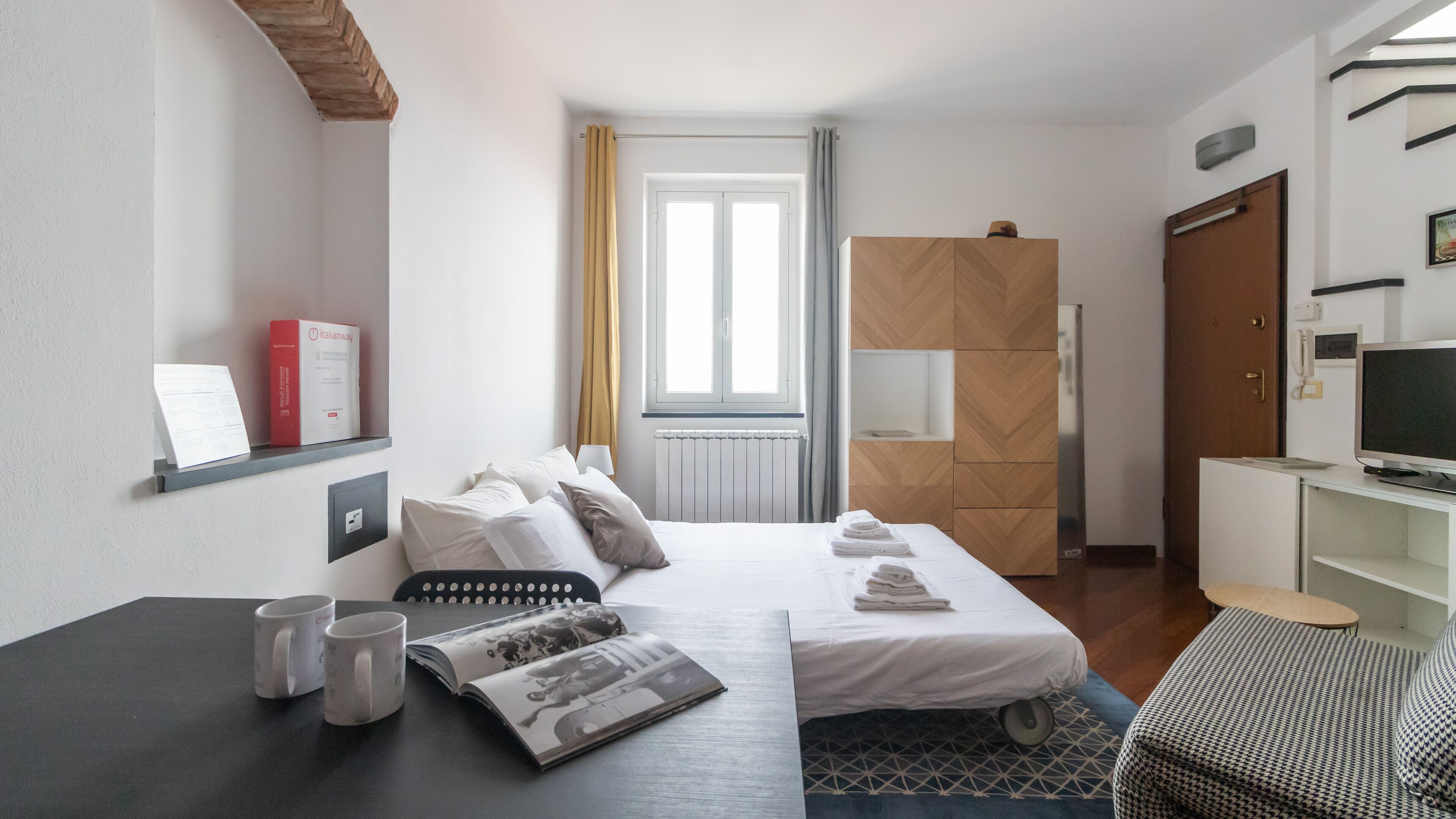 Una camera d'albergo con un letto, una scrivania con un portatile, una sedia, una televisione e un armadio.