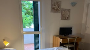 Een slaapkamer met een bed, een bureau, een televisie en een deur naar buiten.