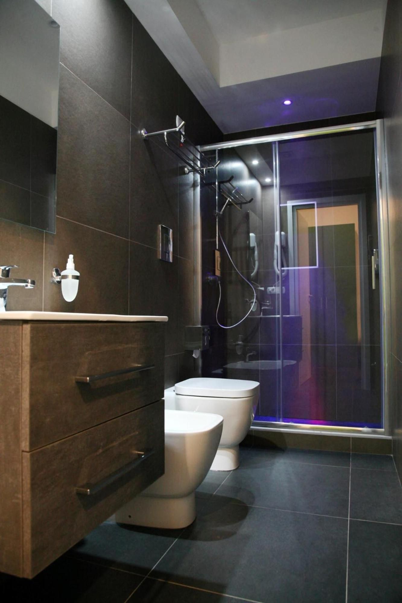 Une salle de bain moderne avec deux toilettes, un espace douche et un carrelage foncé.