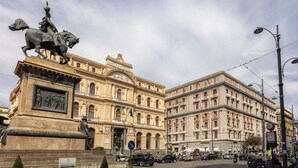 Un edificio histórico con arquitectura clásica, una estatua destacada y una calle concurrida.