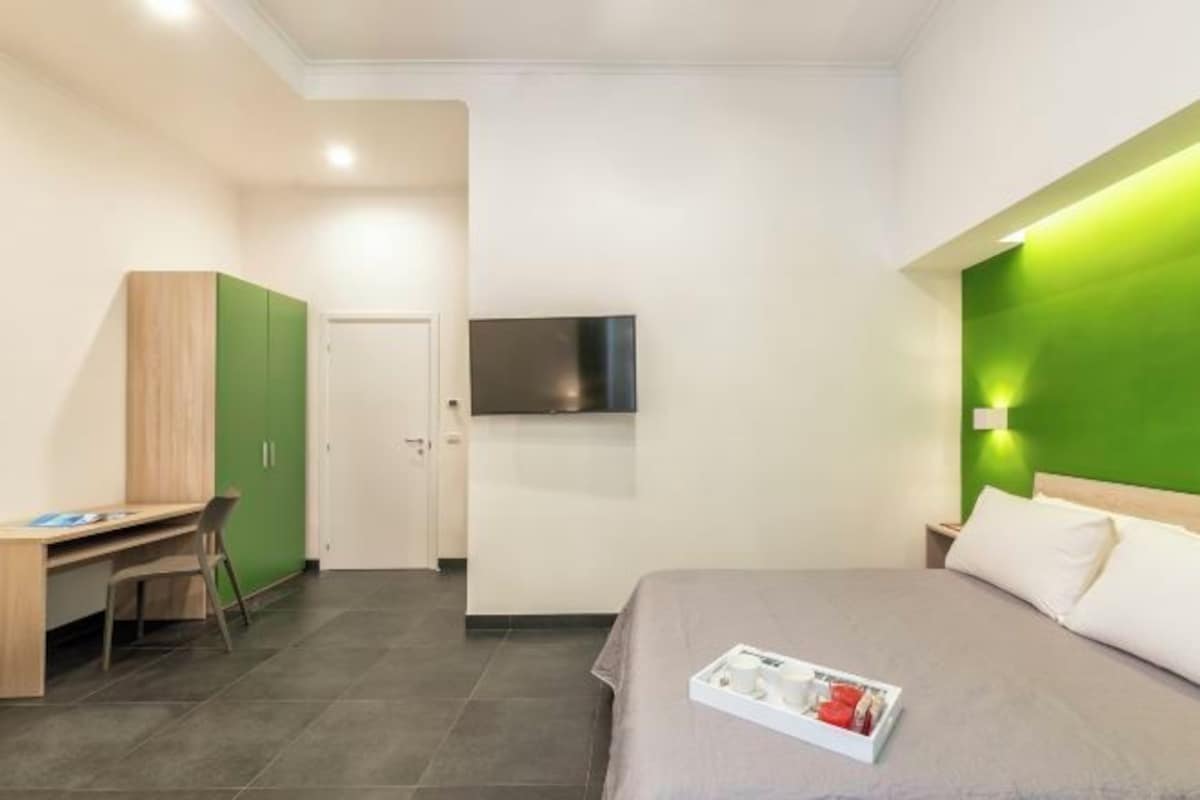 Una habitación de hotel moderna con cama, escritorio, televisor y una pared de acento verde.
