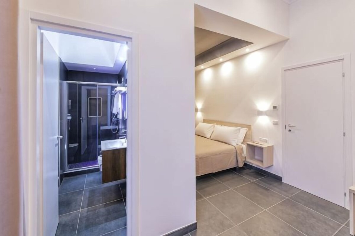 Una habitación de hotel con ducha, cama, mesita de noche y tocador.