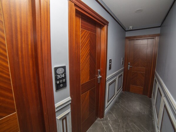 Un pasillo con puertas de madera, un panel de control de ascensor en la pared y suelo de mármol.