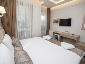 Ein Hotelzimmer mit Bett, Schreibtisch, Fernseher und einem Fenster mit Vorhängen.