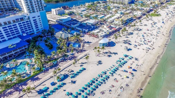 Un complexe hôtelier doté d’une grande piscine, d’une plage avec des parasols et offrant une vue sur l’océan.