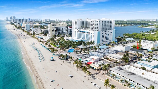 A coastal cityscape with a beachfront hotel featuring multiple floors, a pool, and a view of the ocean. - Hobe Lofts (Hollywood)