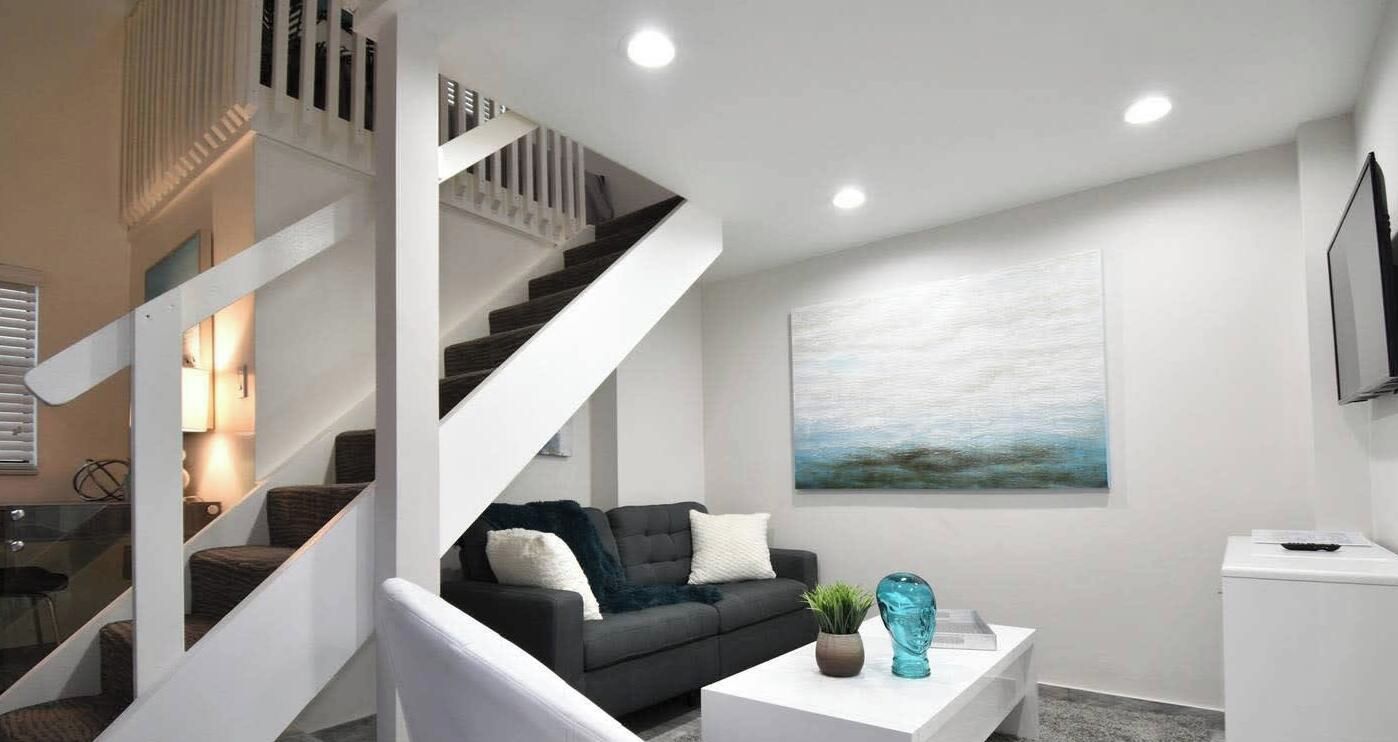 A modern living room with a staircase, a sofa, a coffee table, and a painting on the wall.