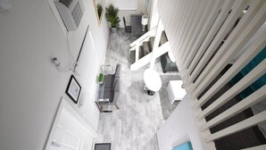 A narrow hallway with a staircase leading to a landing. There is a small seating area with a table and chairs, a potted plant, and a white door at the end of the hallway. - Hobe Lofts (Hollywood)