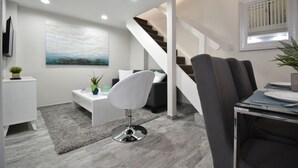 A modern living room with a staircase, a dining area, and a seating area with a sofa and a white chair. - Hobe Lofts (Hollywood)
