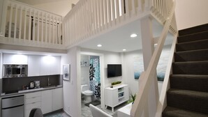 A modern kitchen with a microwave, stove, and sink, a dining area with a table and chairs, and a staircase leading to an upper level. - Hobe Lofts (Hollywood)