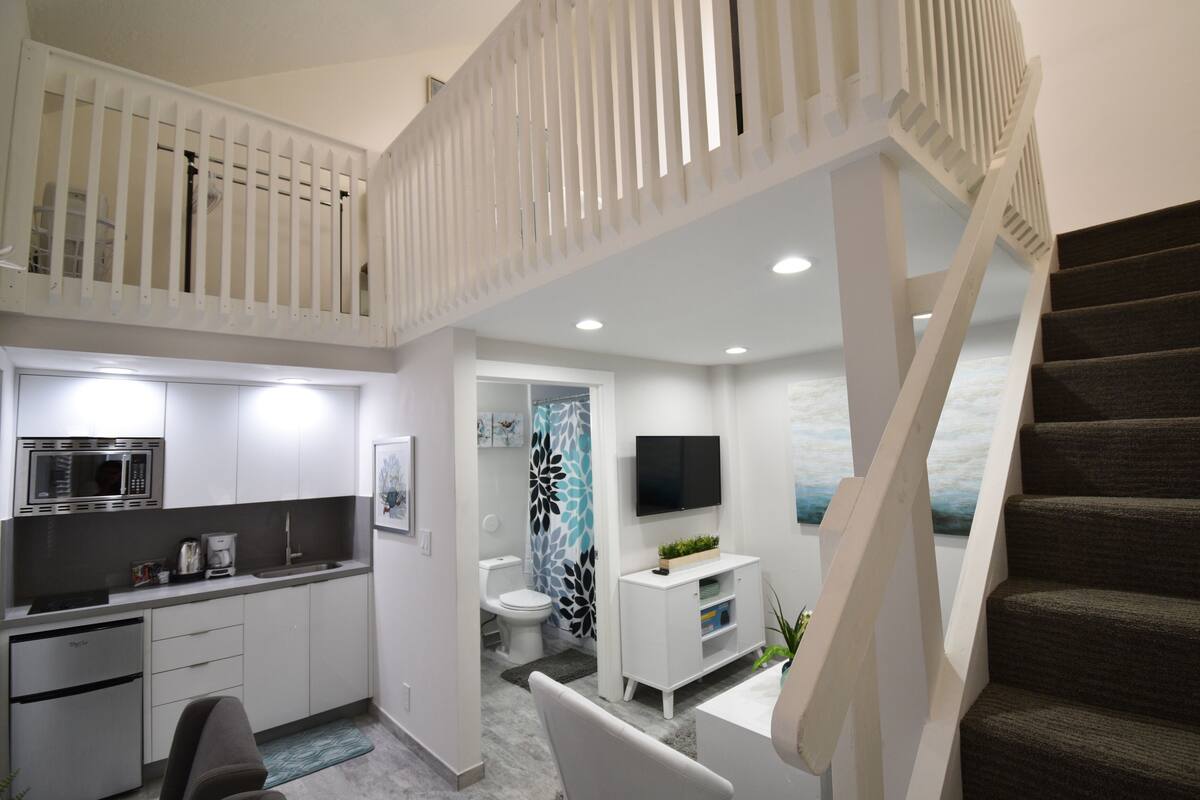 A modern kitchen with a microwave, stove, and sink, a dining area with a table and chairs, and a staircase leading to an upper level.