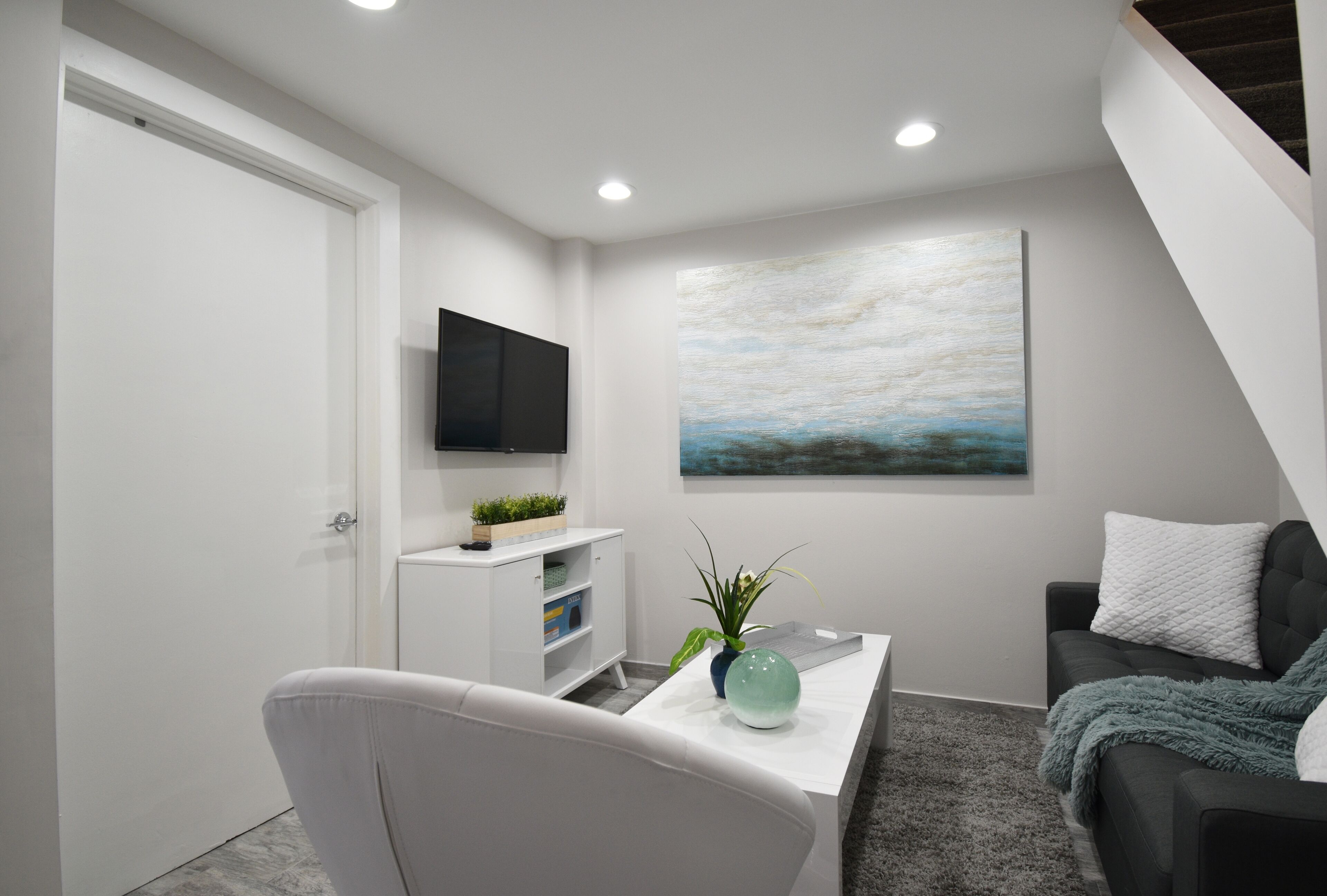 Una sala de estar moderna con un sofá blanco, una mesa de centro con una planta, un televisor de pantalla plana montado en la pared y un cuadro sobre el sofá.