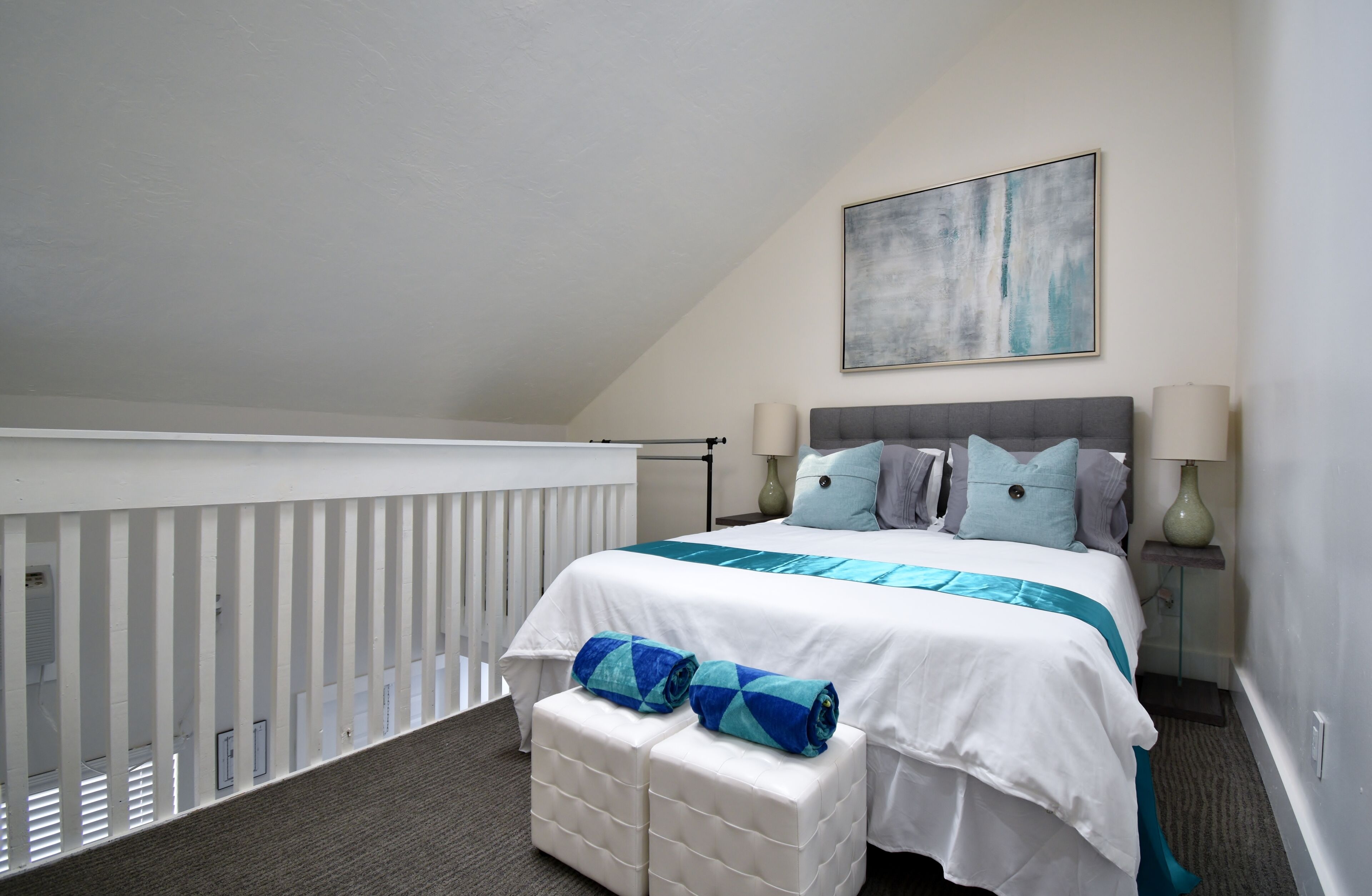 A bedroom with a bed, pillows, a nightstand, a lamp, and a painting on the wall.