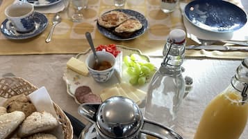 A breakfast setting with a table set for two, including bread, cheese, fruit, and a coffee pot.
