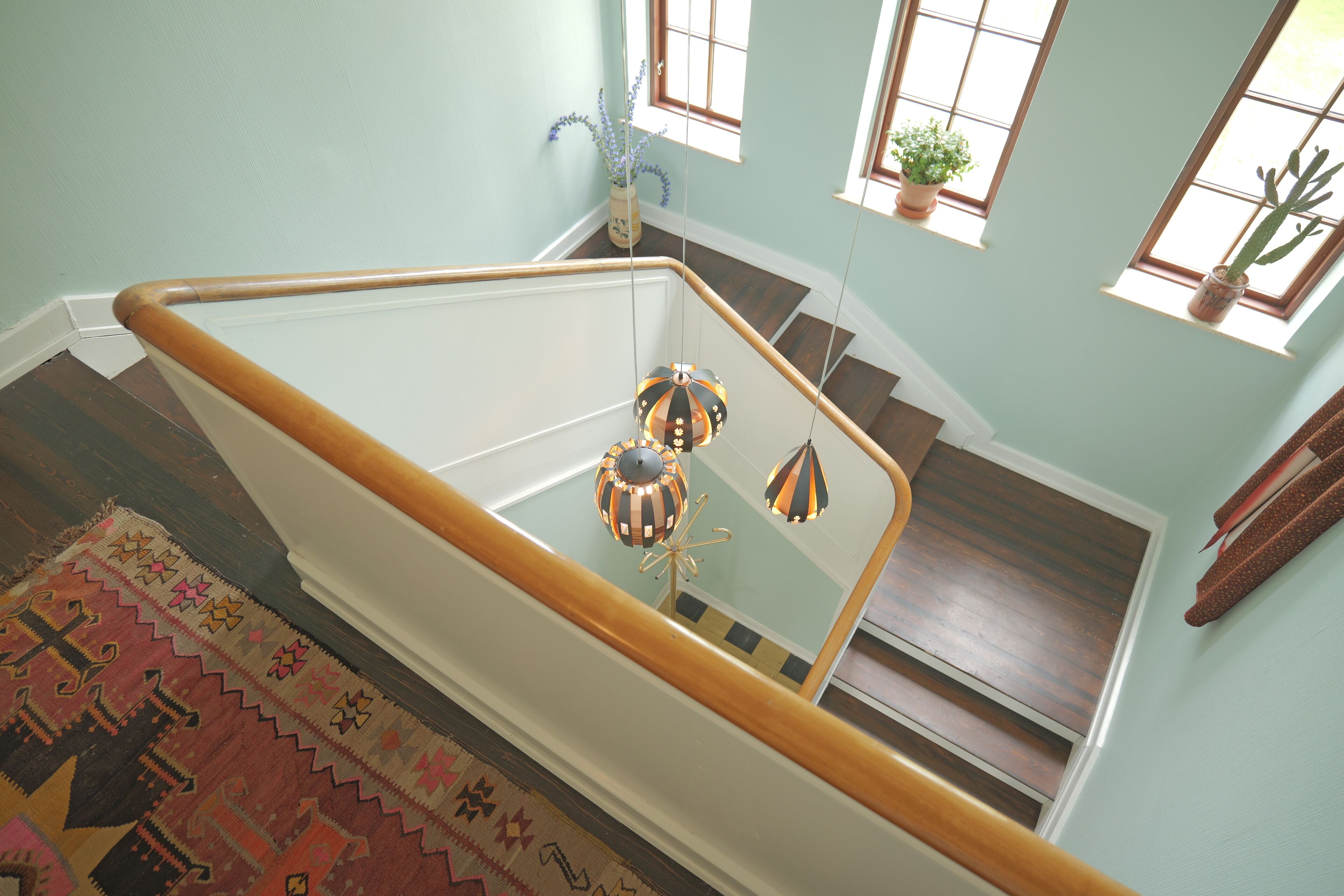A staircase with a wooden handrail, a patterned rug, and a hanging spherical ornament.
