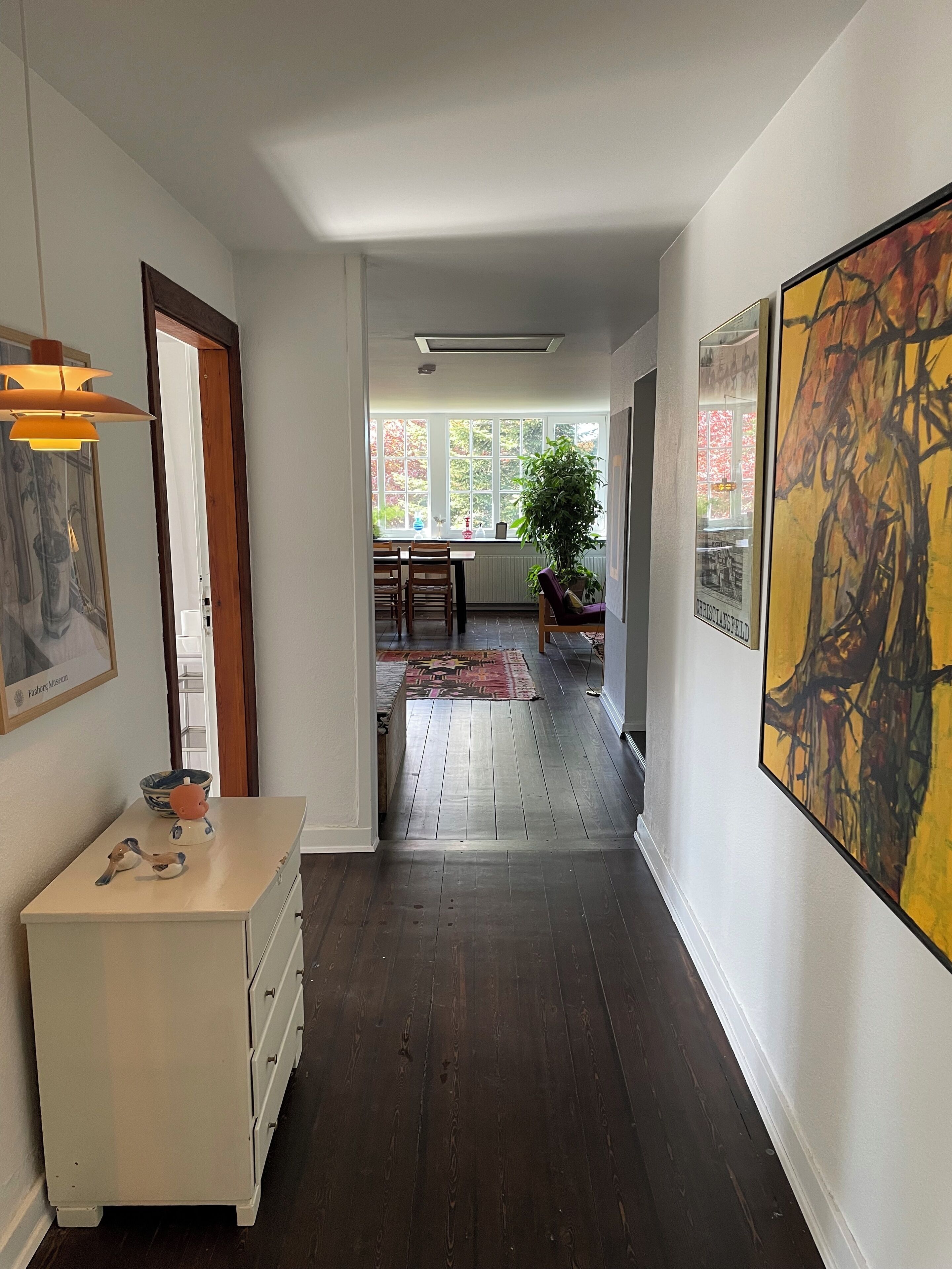 A hallway with a white dresser, a painting, and a large abstract artwork.