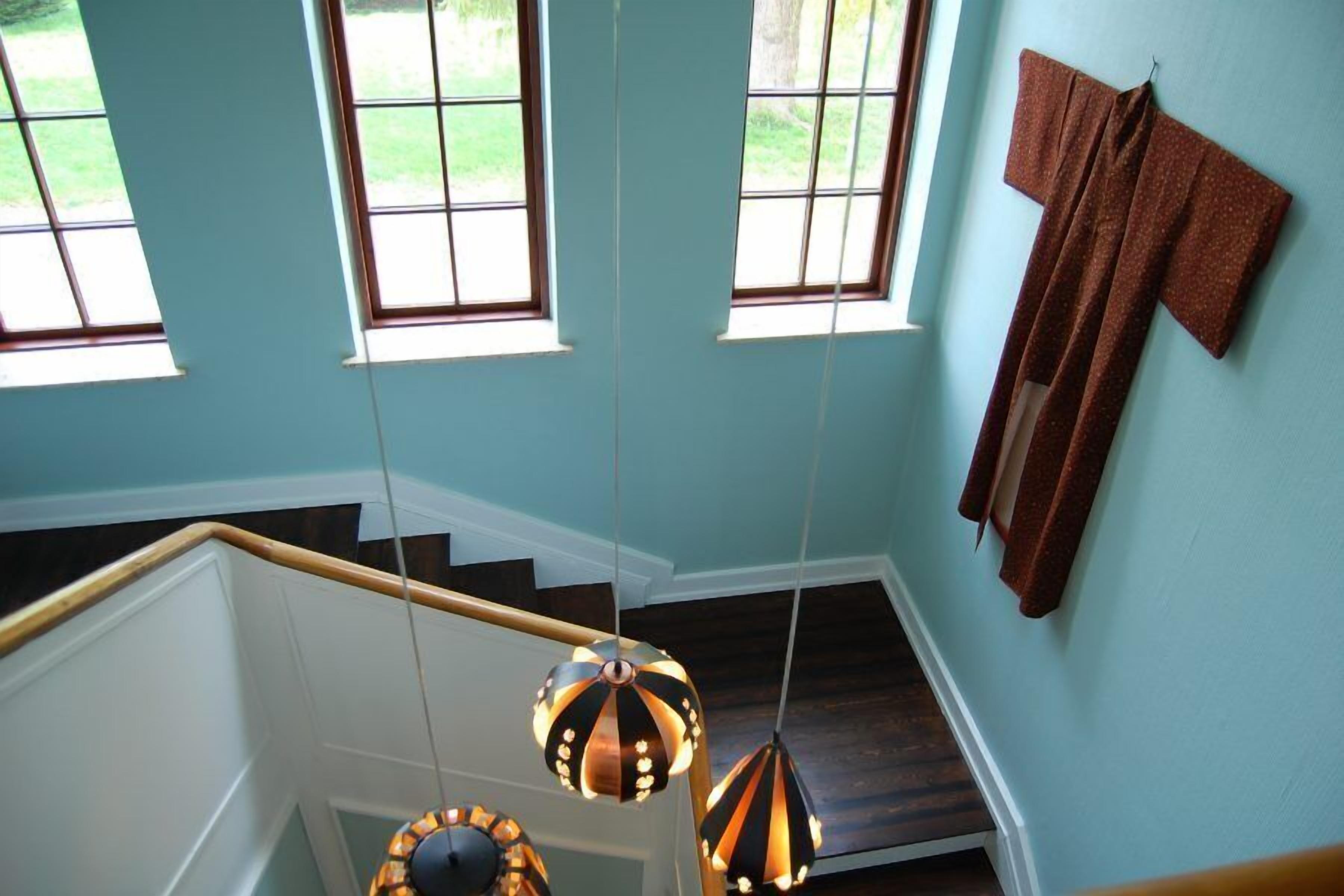 Una escalera con barandilla de madera, una lámpara colgante y una ventana con vista a un jardín verde.