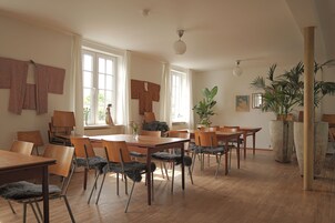 Un'ampia sala da pranzo con tavoli e sedie in legno, ampie finestre e piante in vaso.