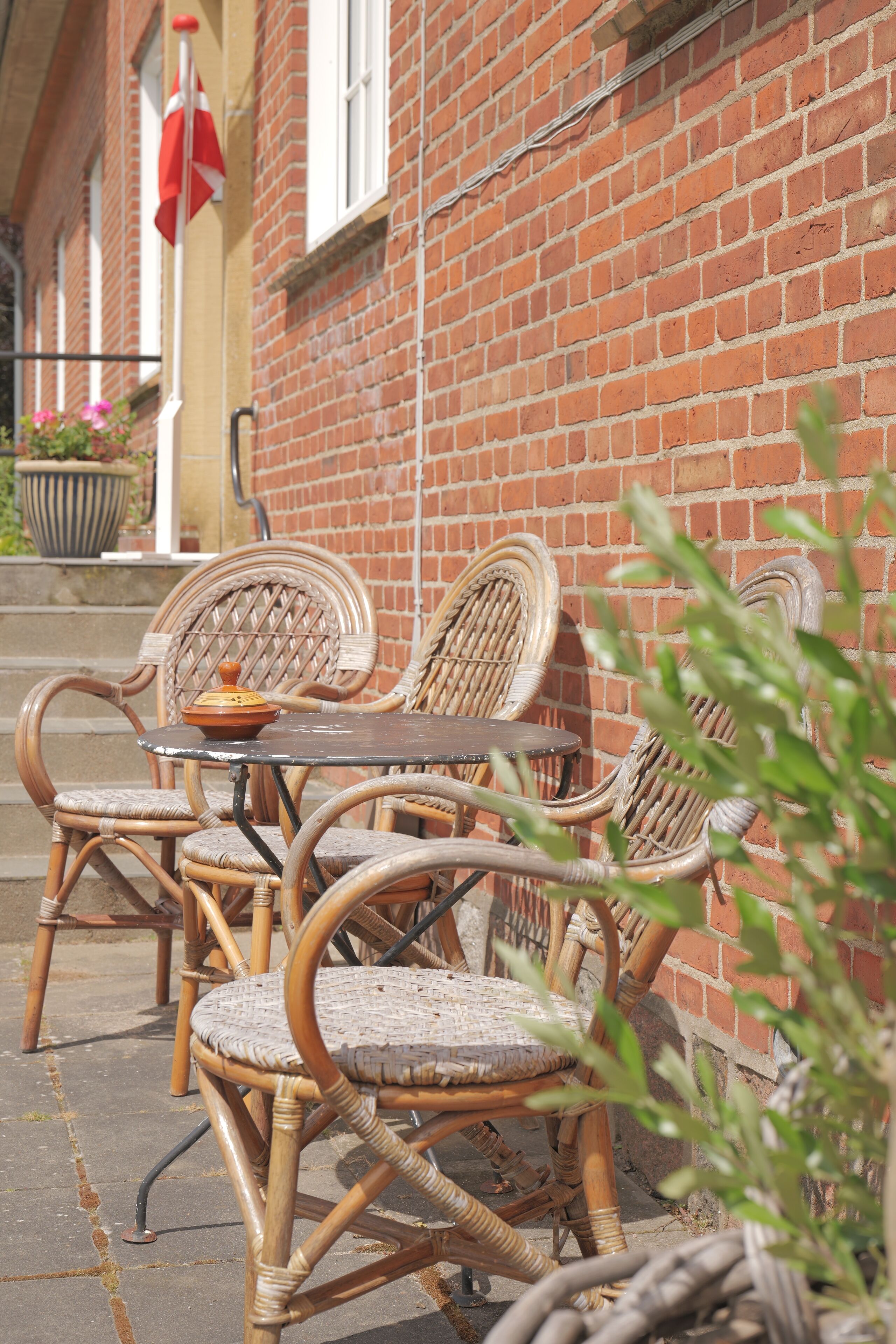 Wicker chairs and a table outside a brick building with a flag.