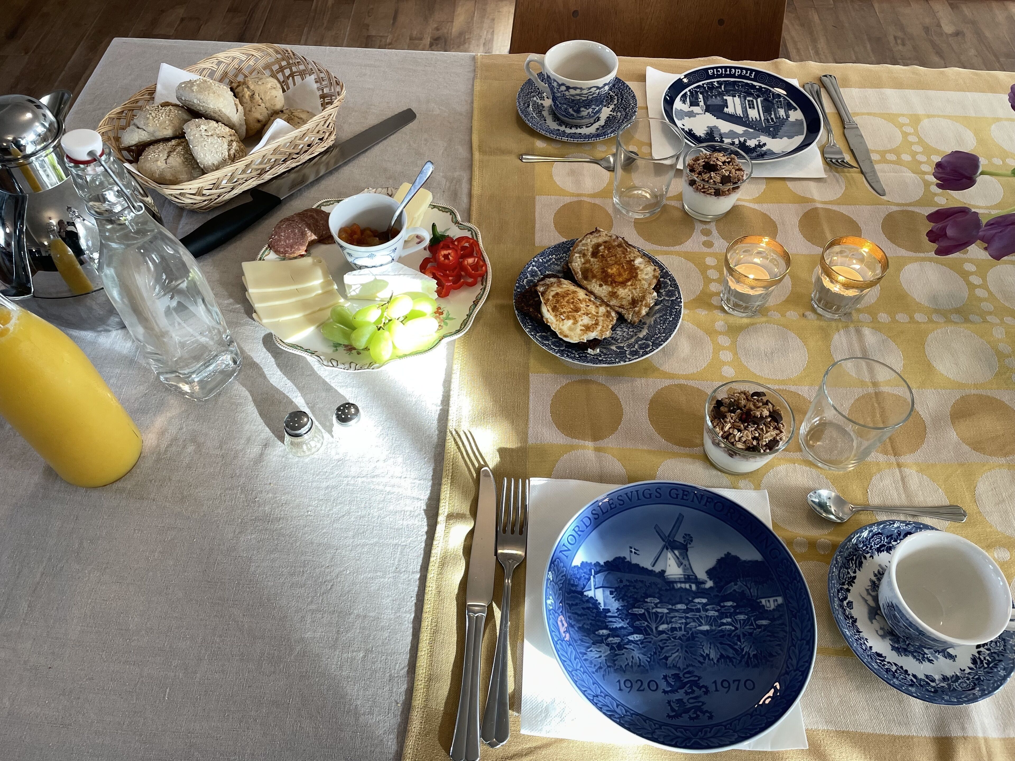 A table set with a variety of dishes, including bread, cheese, grapes, and a plate with a windmill design.