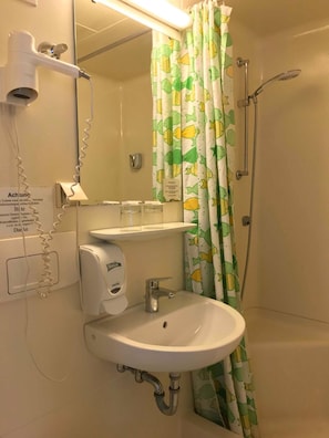 A bathroom with a sink, mirror, hairdryer, shower, and a curtain with a fish pattern. - Gasthof zur Post (Inning A. Ammersee)