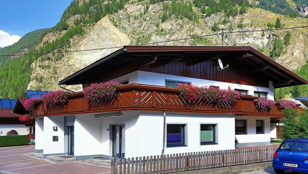 A two-story building with a wooden balcony, a white facade, and a mountain backdrop.