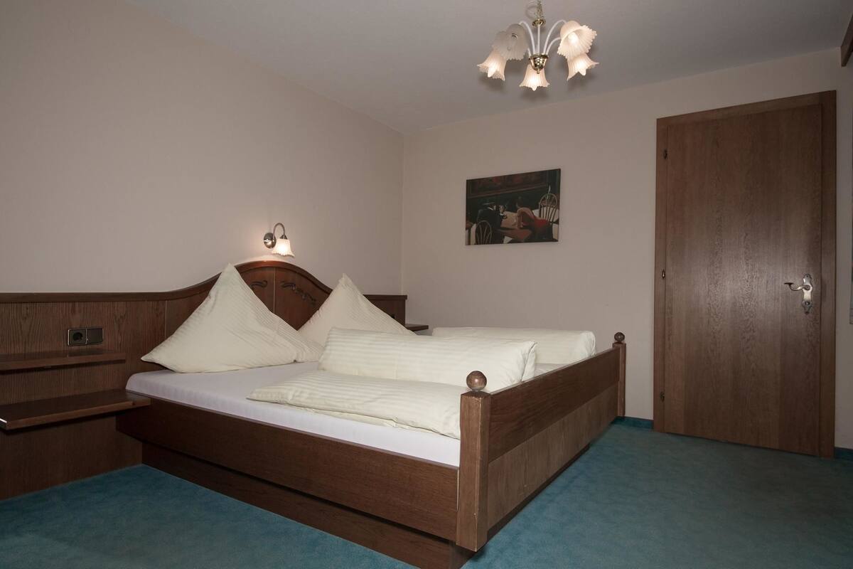 A bedroom with a wooden bed, a nightstand, a wall-mounted lamp, and a door.