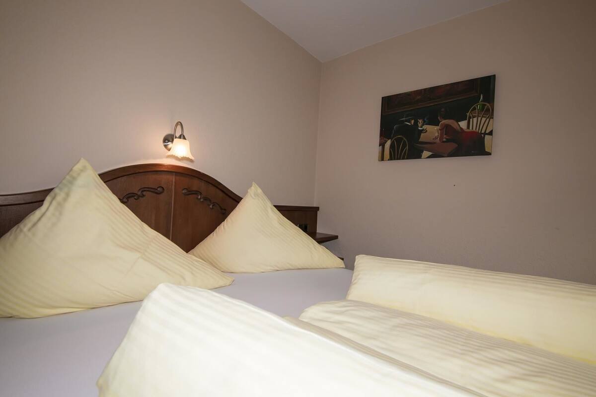 A bedroom with a wooden headboard, a bedside table, a lamp, and a painting on the wall.