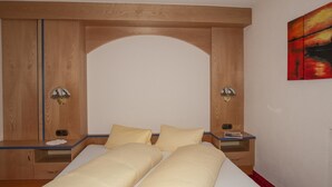 A bedroom with a large bed, two bedside tables, a wooden wardrobe, and a painting on the wall.