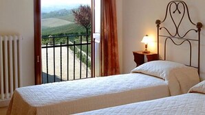 Een slaapkamer met twee bedden, een balkon met uitzicht op het platteland en een nachtkastje met een lamp.