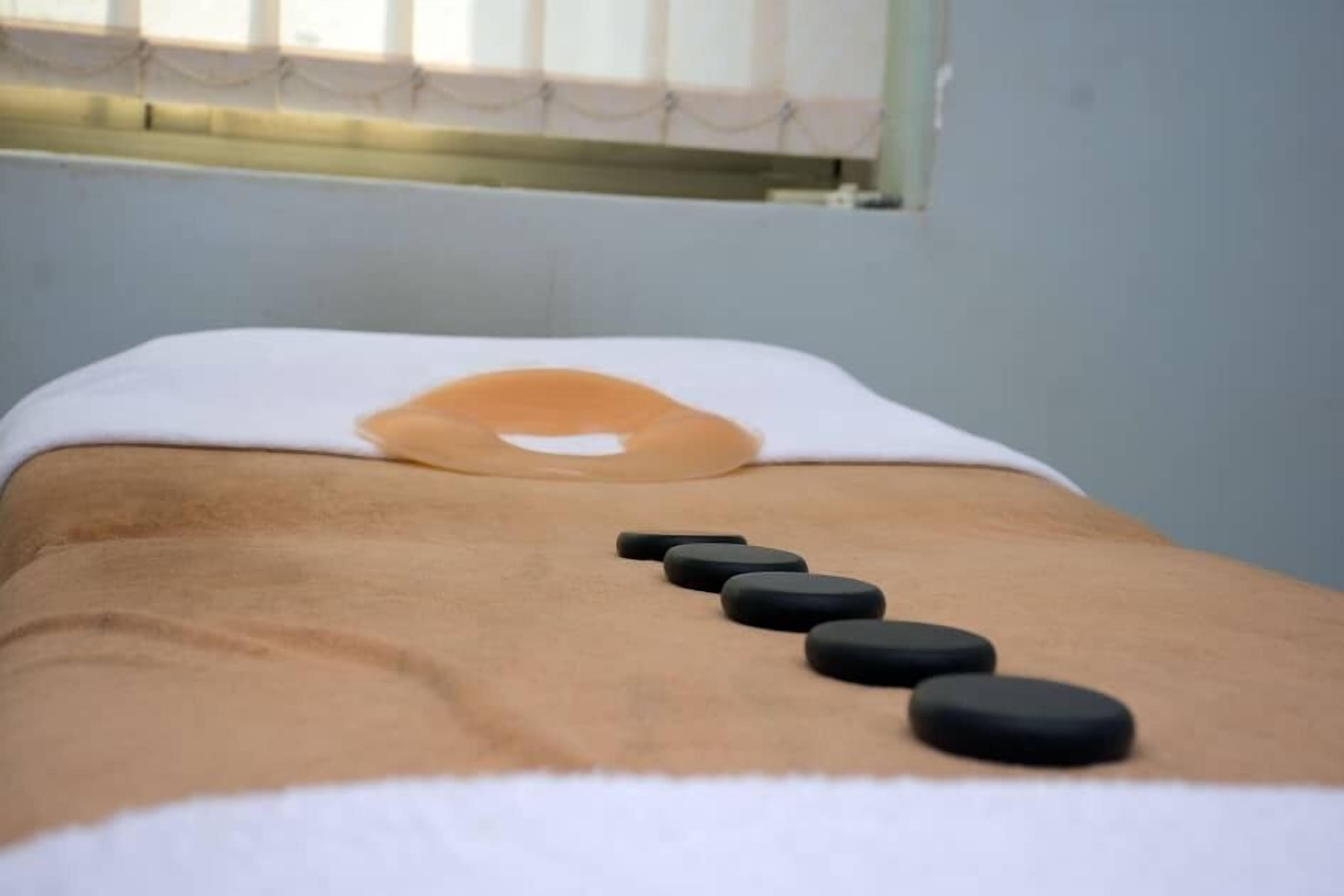 A massage therapy room with a massage table, a white towel, and black massage stones.