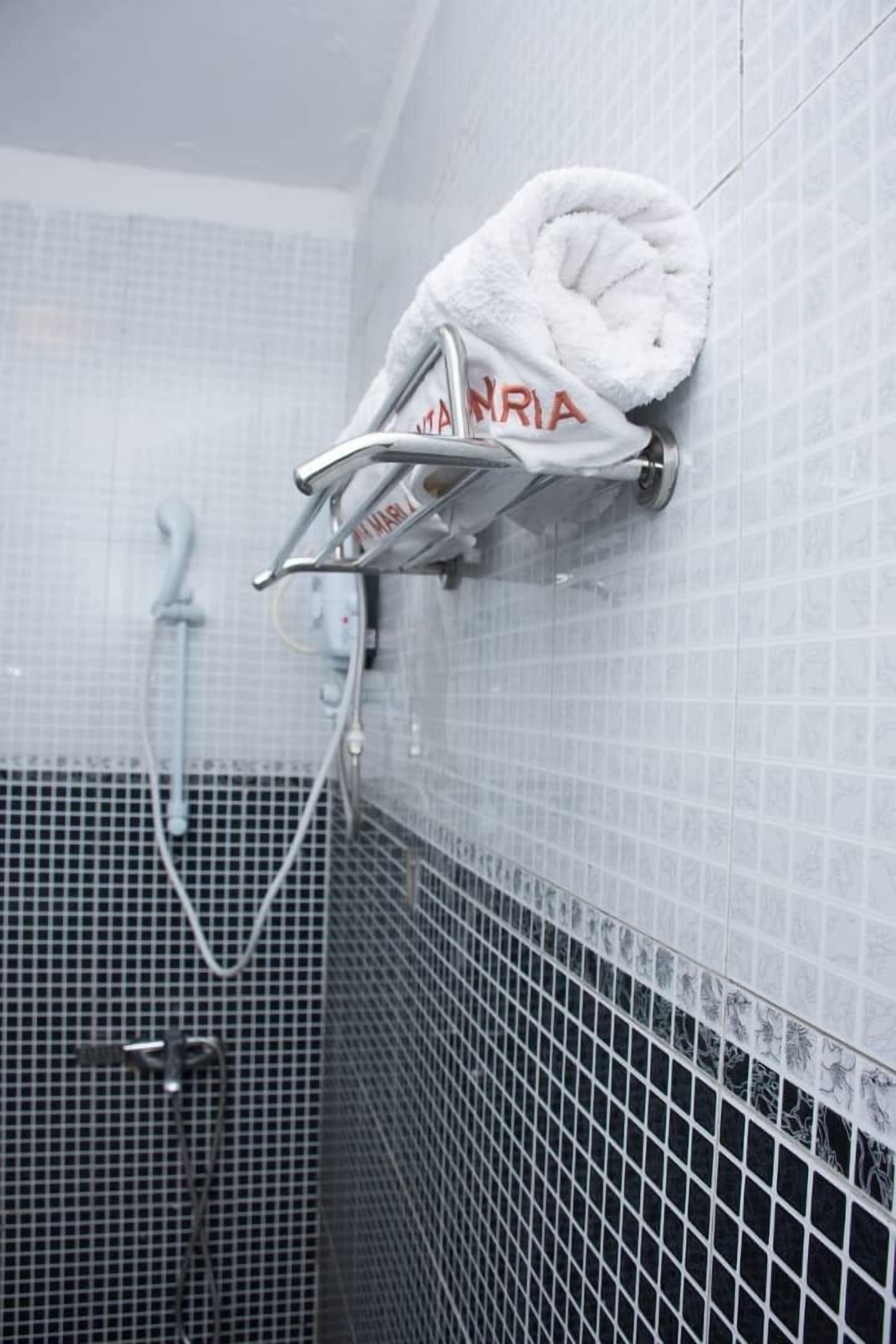 A bathroom with a white towel rack holding a towel with "MARRIA" written on it, a shower head, and a tiled wall.