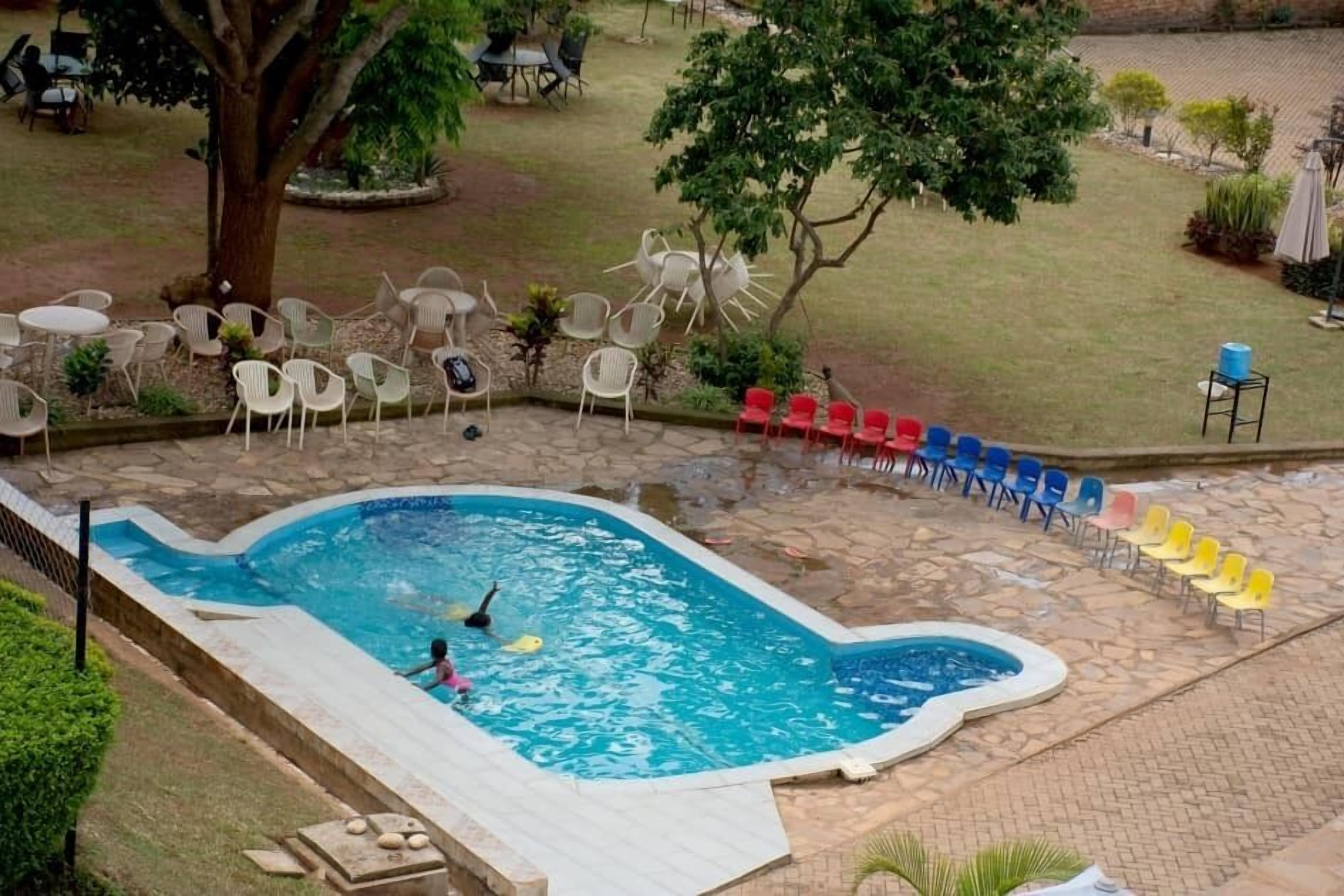 Una piscina con borde de piedra, rodeada de mobiliario exterior y árboles.
