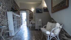 A hallway with a stone wall, a white cabinet, a wicker chair, and a white sofa. - Domo Sa Barra (Sant'Antioco)