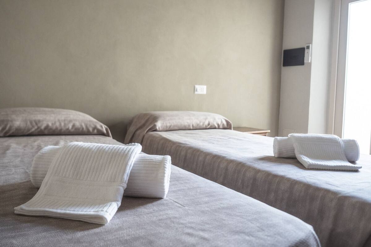 A hotel room with two beds, each with a white pillow and a folded white towel.