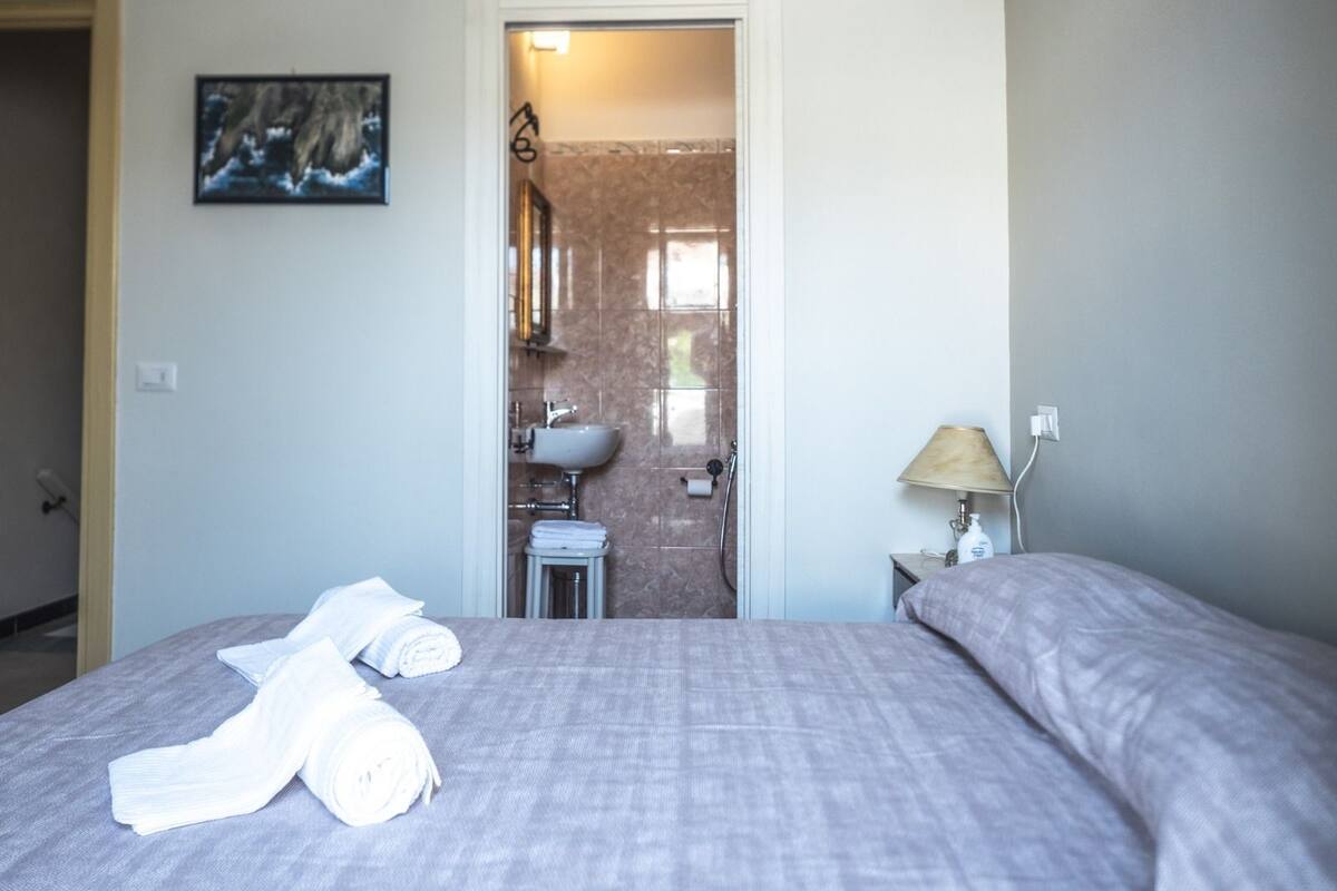 A bedroom with a bed, a bedside lamp, and a bathroom visible through an open door.