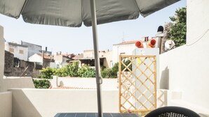 A rooftop terrace with a table and chair, a wooden gate, and a view of surrounding buildings. - Domo Sa Barra (Sant'Antioco)