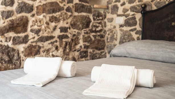 A bed with neatly folded white towels and a stone wall in the background. - Domo Sa Barra (Sant'Antioco)