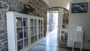 A hallway with a stone wall, a white cabinet with glass doors, a tiled floor, and a door leading to another room. - Domo Sa Barra (Sant'Antioco)