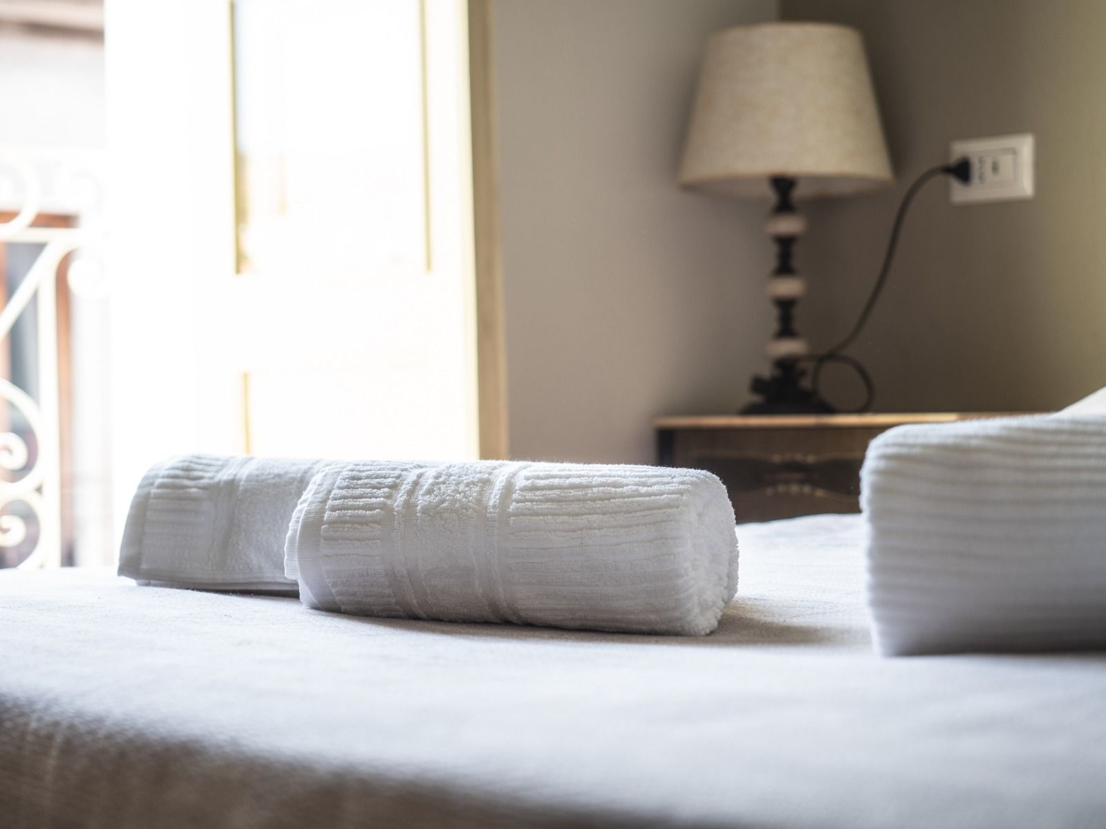 A neatly made bed with two rolled-up towels and a lamp on a bedside table.