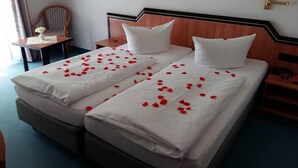 A double bed with white linens and rose petals scattered across the bedspread.