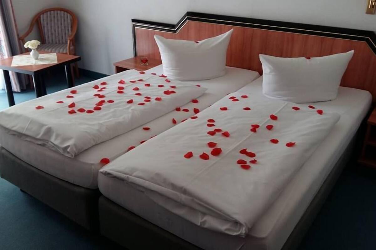 A double bed with white linens and rose petals scattered across the bedspread.
