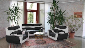 A reception area with a black and white sofa set, a coffee table, and two potted plants. A reception sign is visible on the wall.