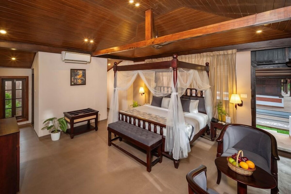 A bedroom with a four-poster bed, a bedside table, a bench, a chair, and a fruit basket.