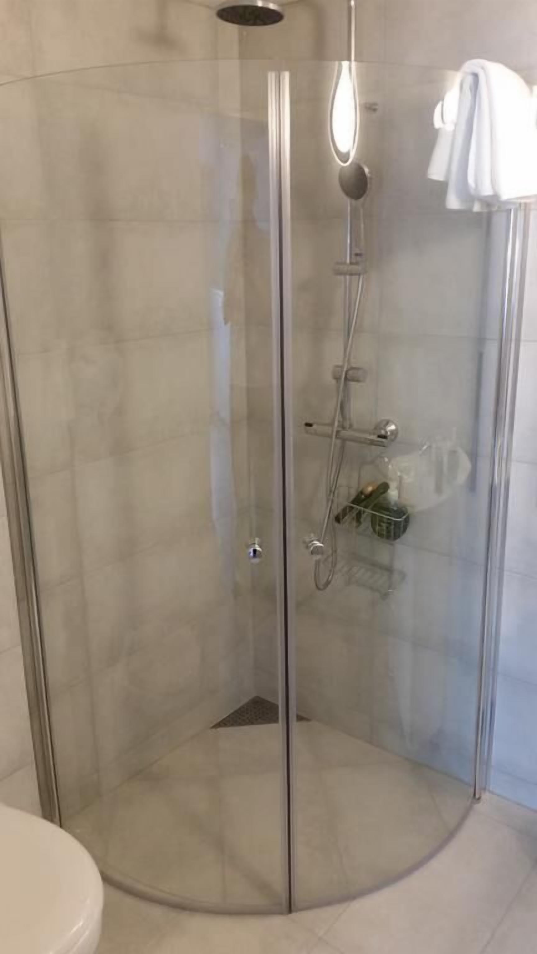 Cabina de ducha con paredes de vidrio, cabezal de ducha de mano, grifo empotrado y perchero.