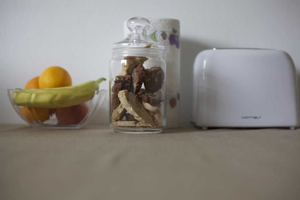 Un frasco con setas secas, un cuenco con frutas y un tostador blanco sobre una mesa.