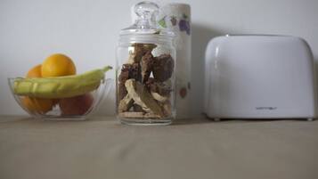 Un frasco con setas secas, un cuenco con frutas y un tostador blanco sobre una mesa.
